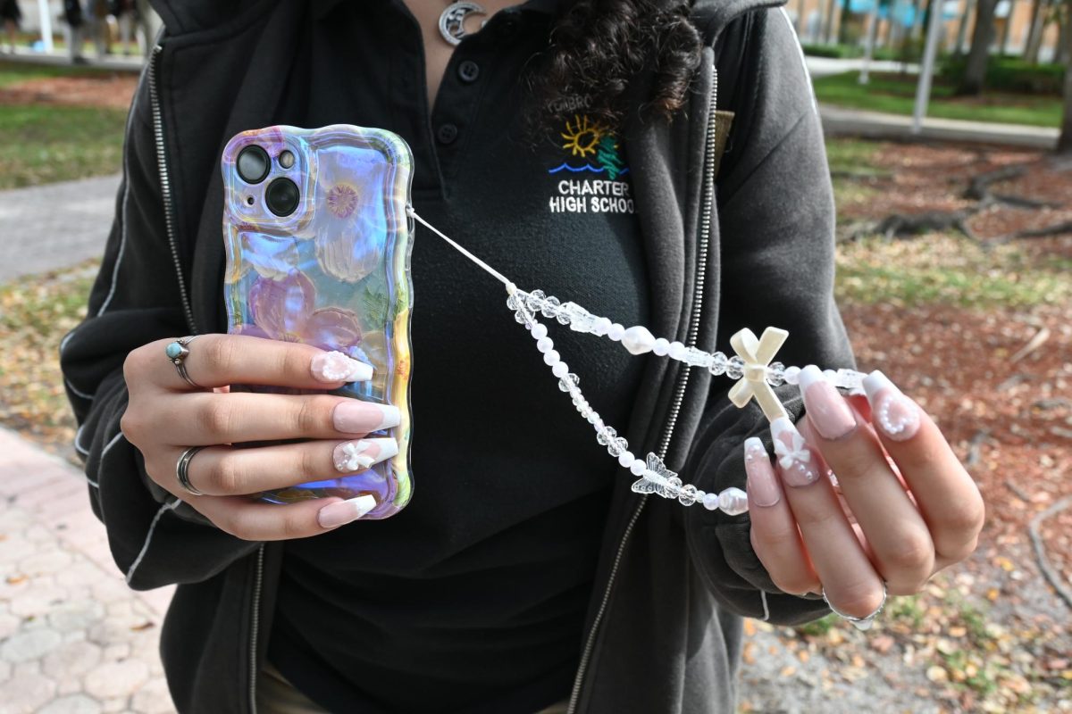 A student showcases their take on the “coquette” trend with their phone case and phone charm! Following the common theme of bows and pastel colors, the phone charm has an arrangement of varying bows and butterfly beads.