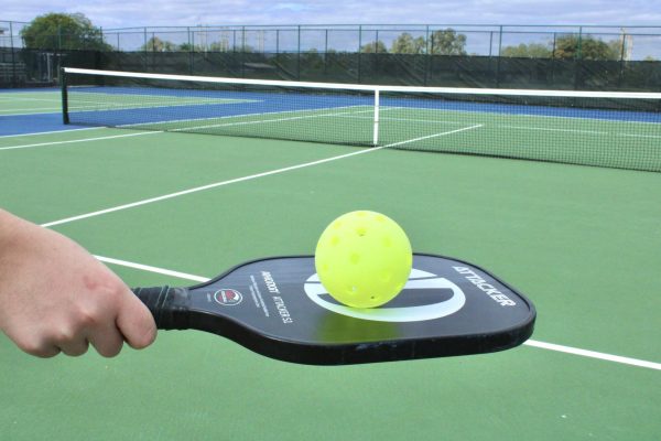 A pickleball rests on a players paddle. But the real story lies in the background: the potential blending of the two  courts (tennis and pickleball) poses much debate around campus. 