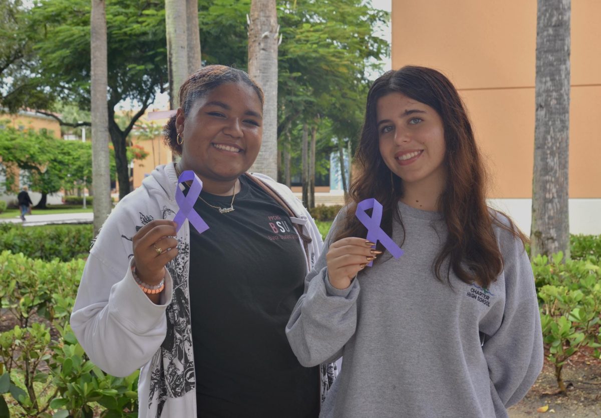 CHAT staff members Juliana Duperval and Amaya Jorge stand outside holding a purple ribbon, the nationally recognized symbol for domestic violence awareness month.