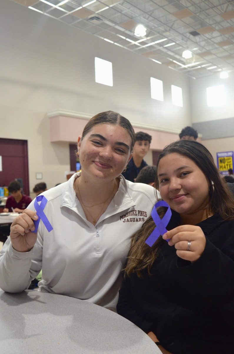  PPCHS students Cassandra Smith and Sabrina Royero hold the purple ribbons in the cafeteria, doing their part in representing awareness for domestic violence