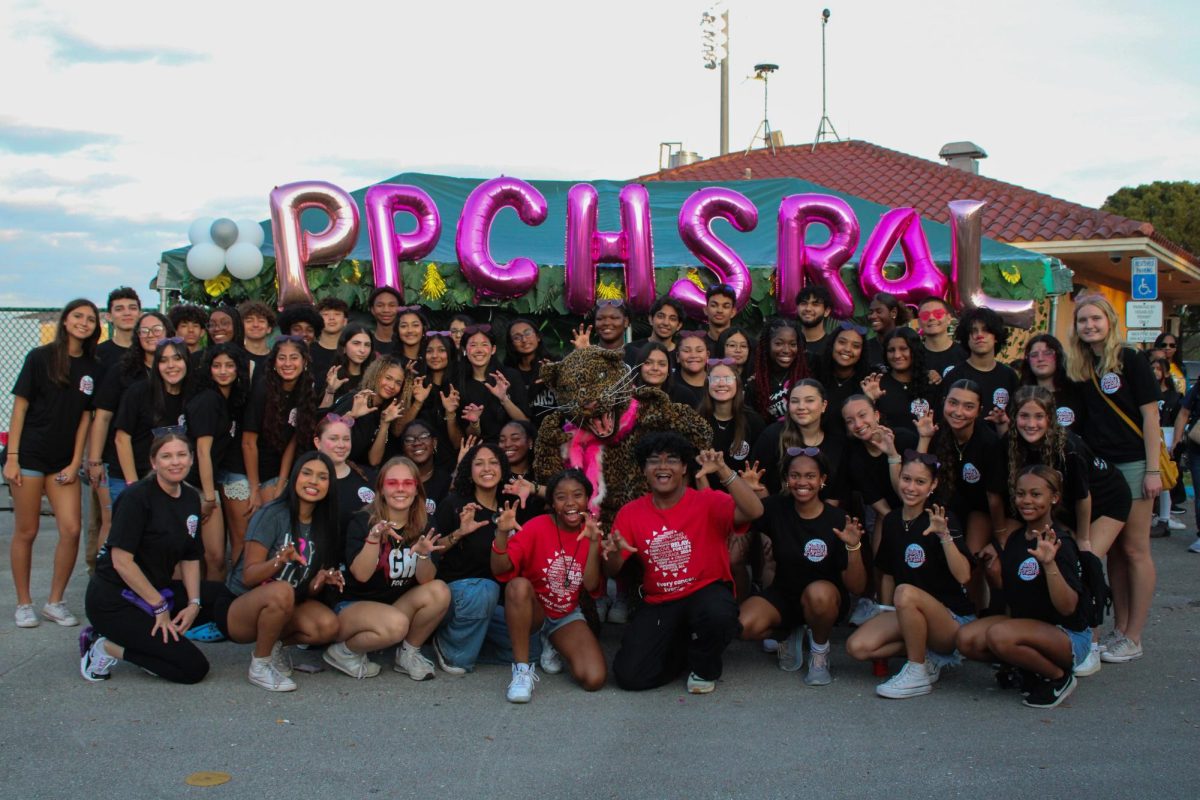 The PPCHS Relay For Life team stands near the football field, ready to reprise their 27th annual relay event that raises money for those fighting breast cancer. The balloons behind them are a bright pink, the color representing breast cancer awareness. 