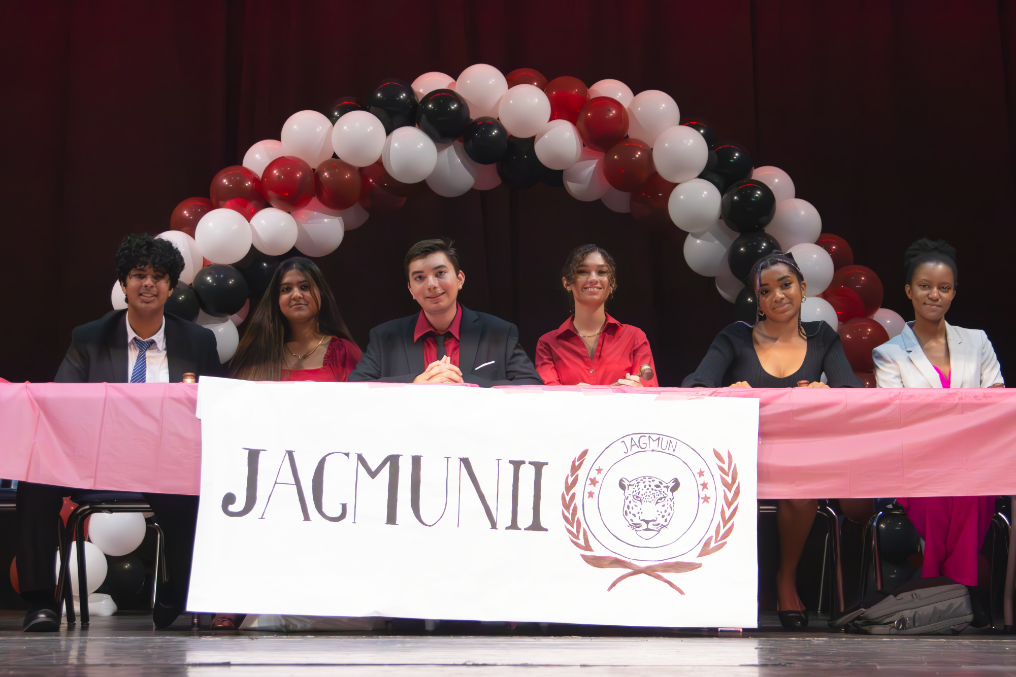 These are the underclassmen board members for Model UN. Starting from the left is sophomore and Assistant GA Director Dev Gupta, then junior and Secretary Nusaybah Arif, next to her is junior and Treasurer Alejandro Agudelo, then is junior and Assistant Crisis Director Yasmin Dominguez, next junior and Head Crisis Director Brooke Wooden, and finaly on the complete right is junior and Parliamentarian Mikayla Hines. These board members are sitting on the River of Grass Auditorium Stage welcoming students participating in JAGMUN with a beautiful handmade banner.
