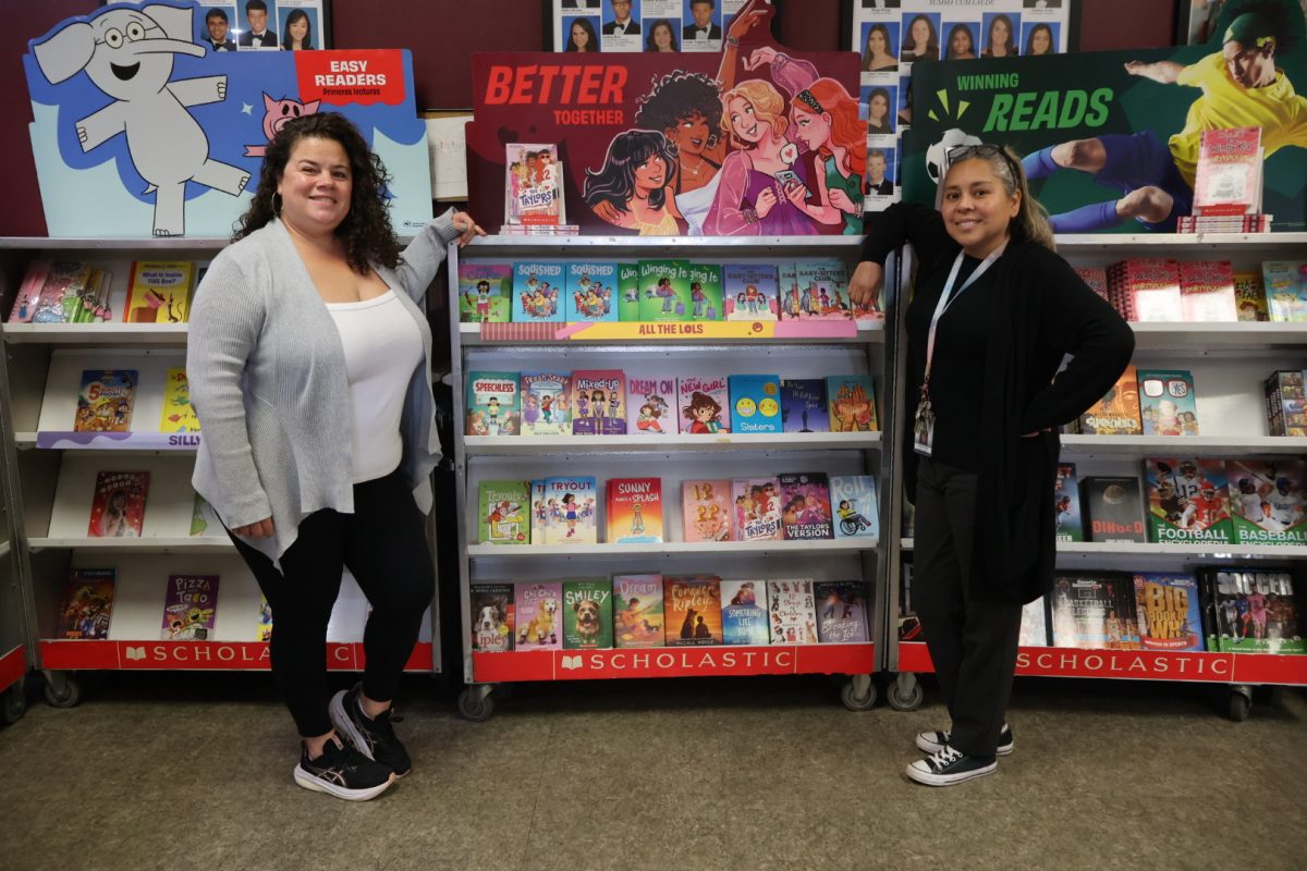 Priscilla Chaca (right) and Yasmin Martinez (left), members of PPCHS's Media department, stand at the PPCHS Scholastic book drive, where students could purchase children's books and donate them to those in need. In addition to their work in the Media department, the two manage PPCHS's alumni page, working both in outreach and in highlighting former students' achievements.