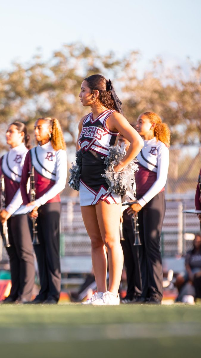 Junior cheerleader, Gabriella Ganen  stands on the field at the varsity football game as she cheers on the players as they roar onto the field.
