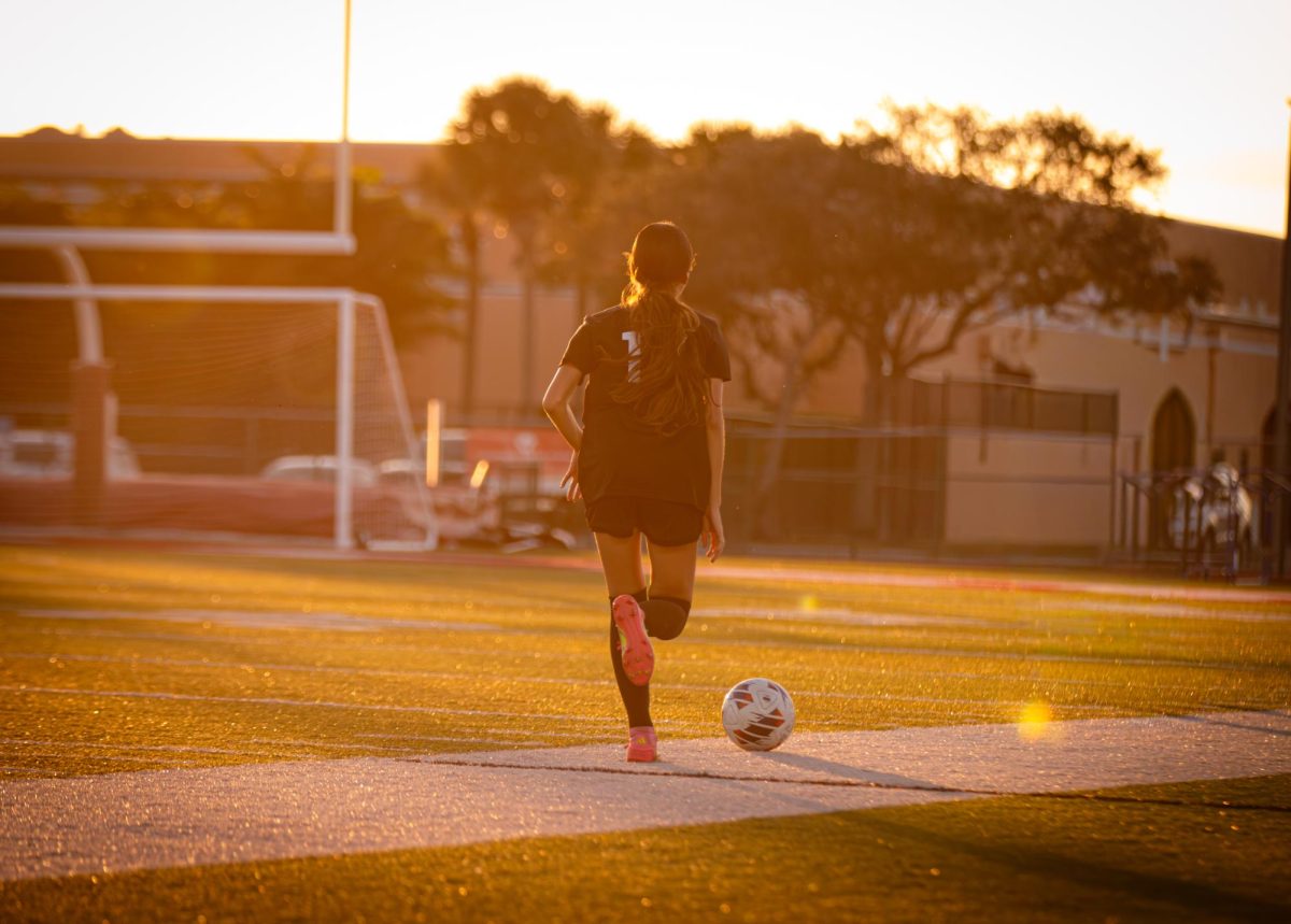 Mia Flores kicks the soccer ball along the sideline during the Lady Jags' home game with the sunset shining on the field.