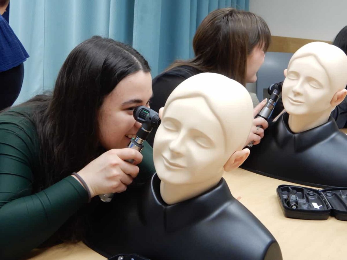 Camilla Penso (center, left) practices an ear exam on a training model during a clinical skills lab, one small step on her path toward becoming a physician.