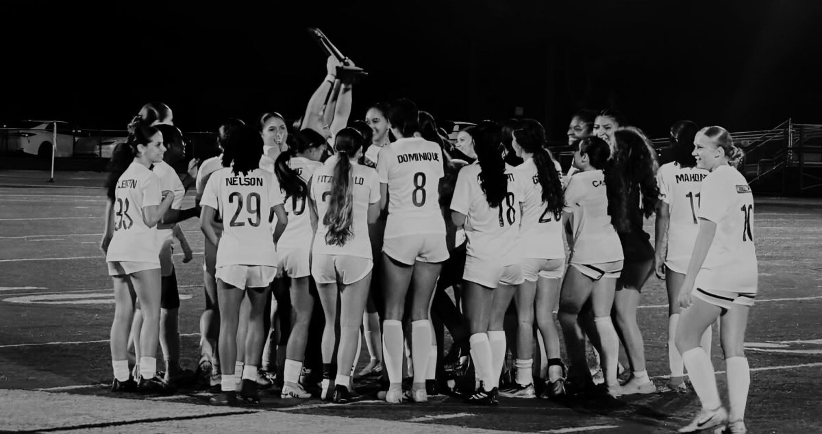 The Lady Jags soccer team stand on the field with the district champion trophy celebrating their victory.