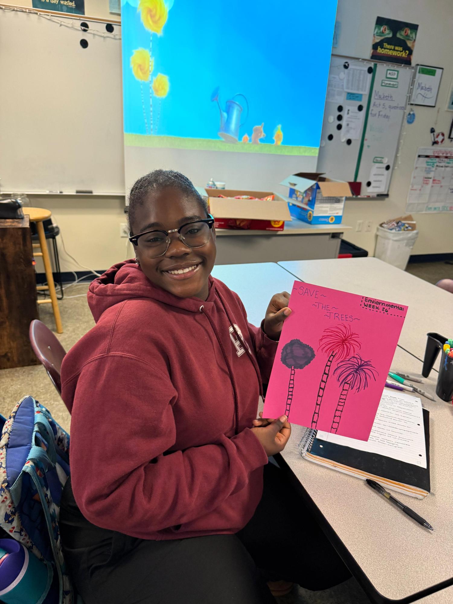 Senior, Kyra Theodore shows her drawing of trees representing the movie playing in the back, "The Lorax". As a way to show her appreciation during environmental week.
