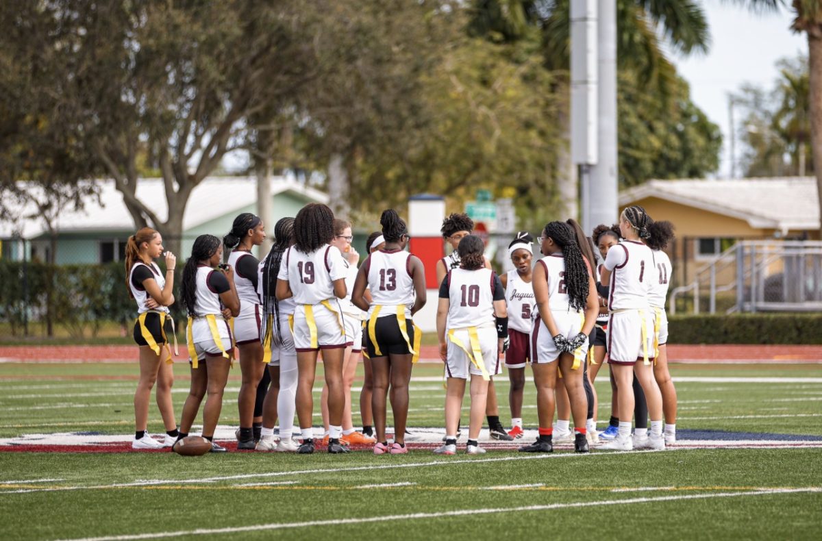The Lady Jags flag football team standing together in a circle listening to their coach's game plan.
