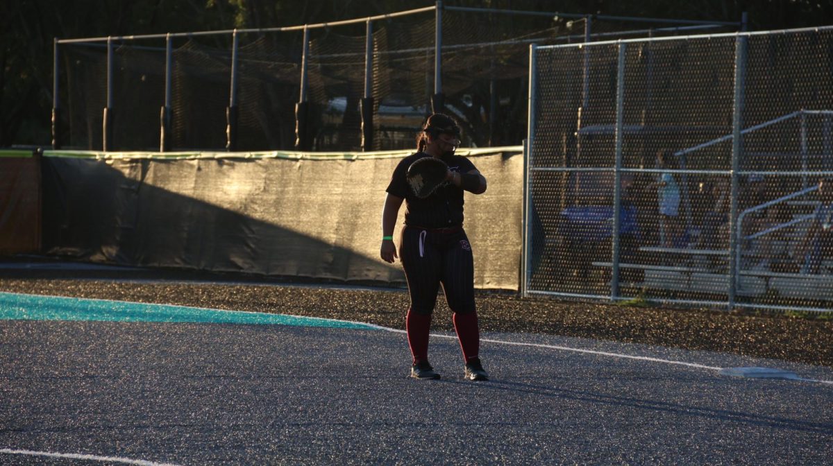 Sophomore Isabella Pascual at first base reading the signs off of her wrist band. The signs indicate which pitch the pitcher is throwing next. 