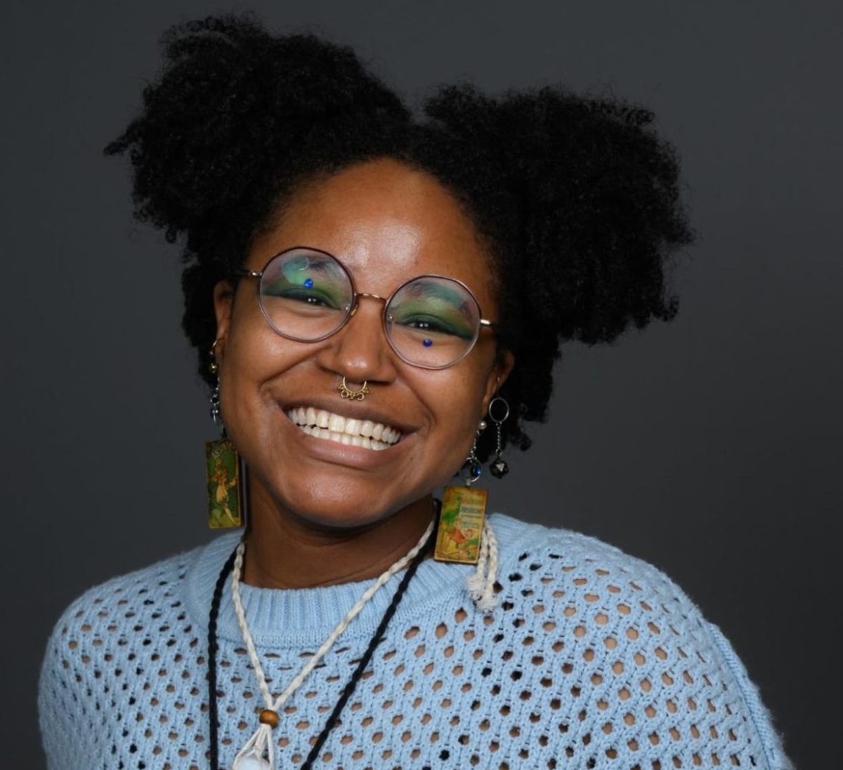  Kaila “Key” Gumbs smiles in a portrait wearing glasses, earrings, and a light blue sweater.
