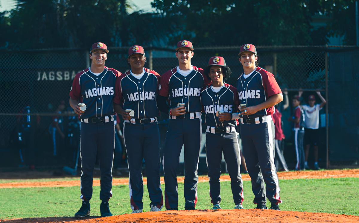 The Jaguar seniors standing together on the pitchers mound smiling for a photo before they pick up the dirt off and add it to their mason cup to hold as a memory. 