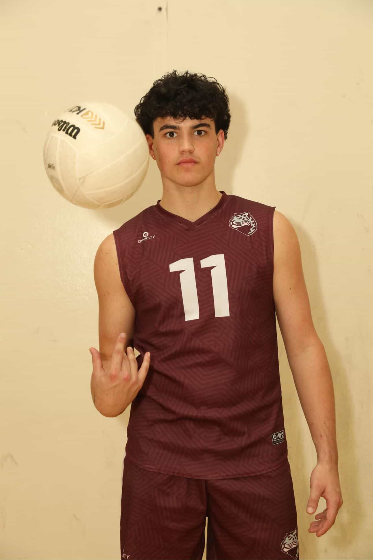 Senior Gerald Cabrera (#11) tossing a volleyball in the air while he poses for his senior photo with his jersey on.