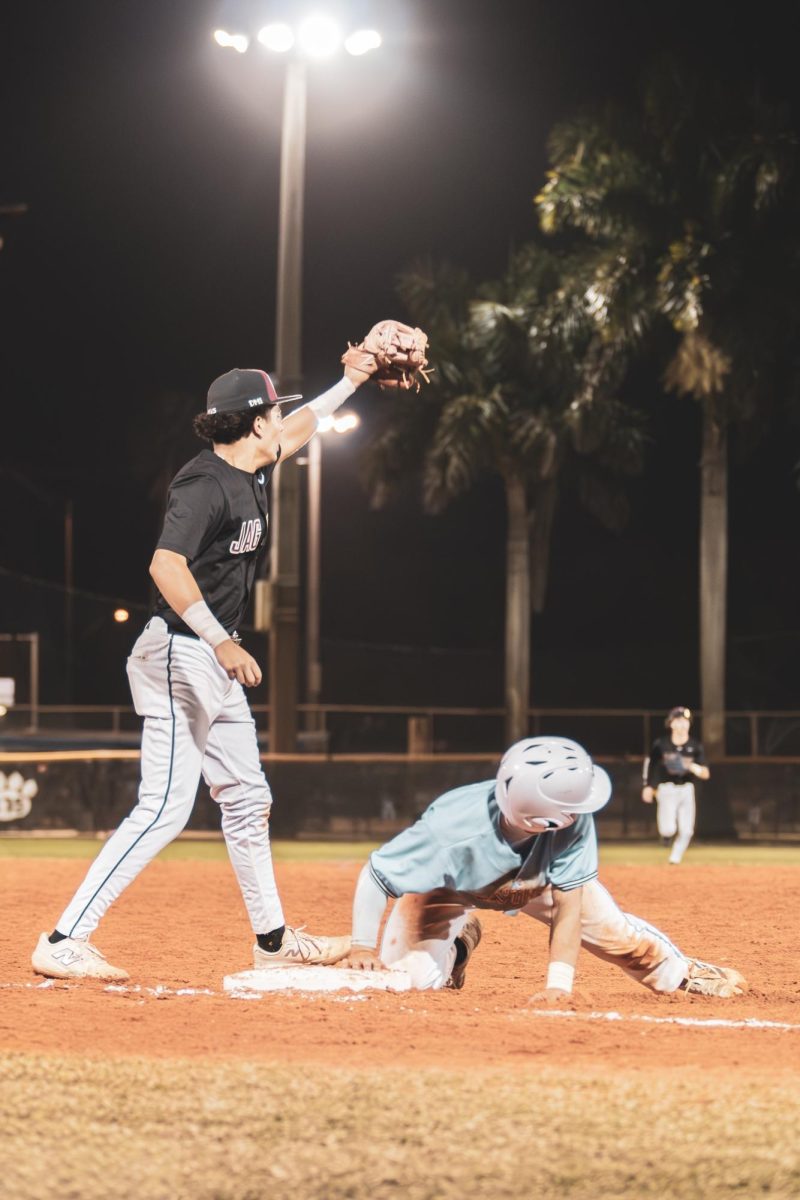 Sophomore Cyrus De Jesus holds his glove in the air waiting for the ball to be thrown to him as a player from the other team slides into third base.
