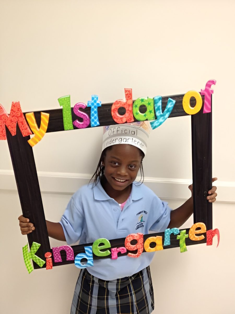 Erioluwa Fatimilehin as a child smiling while holding a frame on her 1st day of kindergarten. 