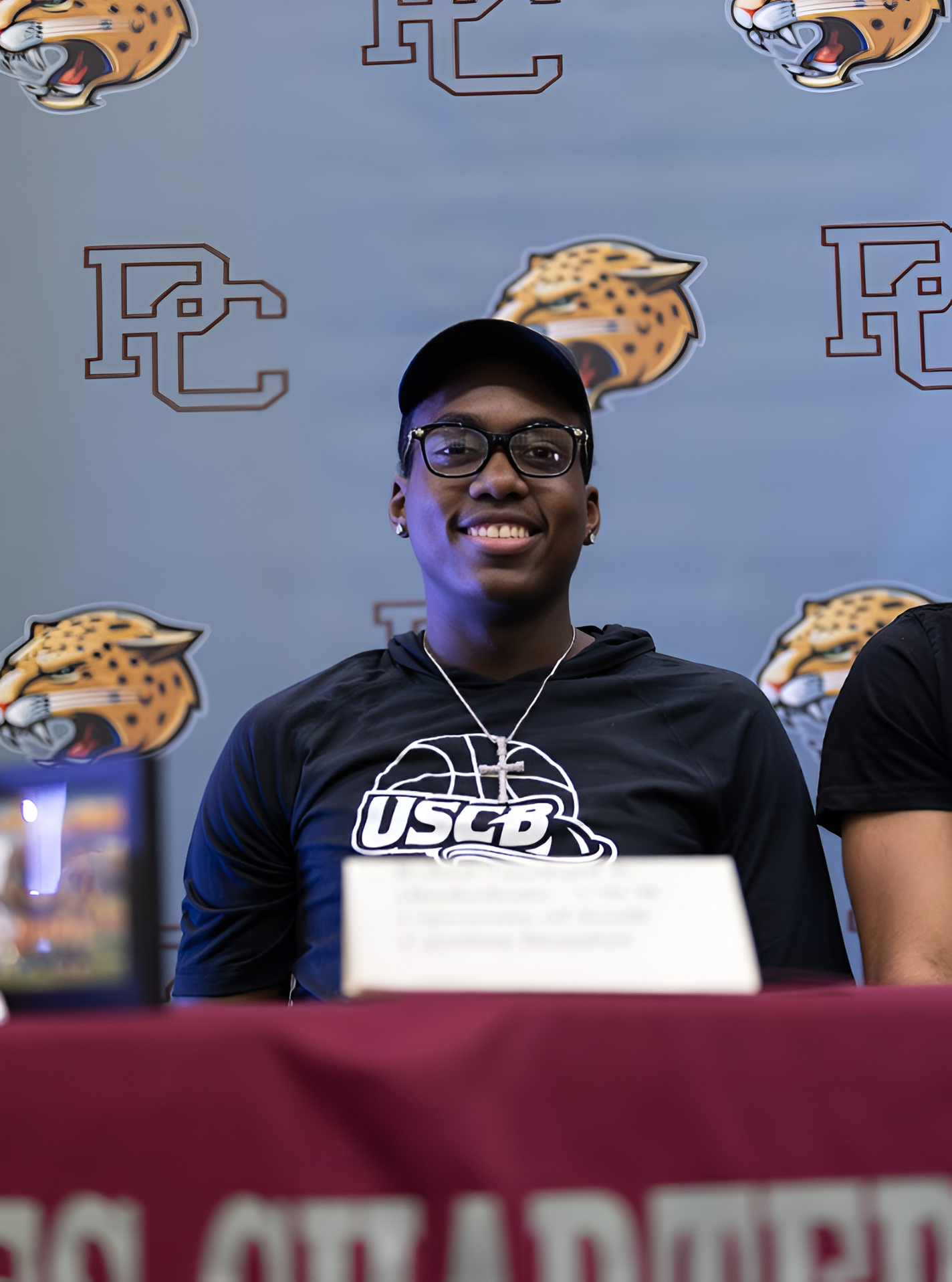 Senior Robert Guishard Jr. smiles at the camera on signing day with a hat and shirt on that represent his future university. 