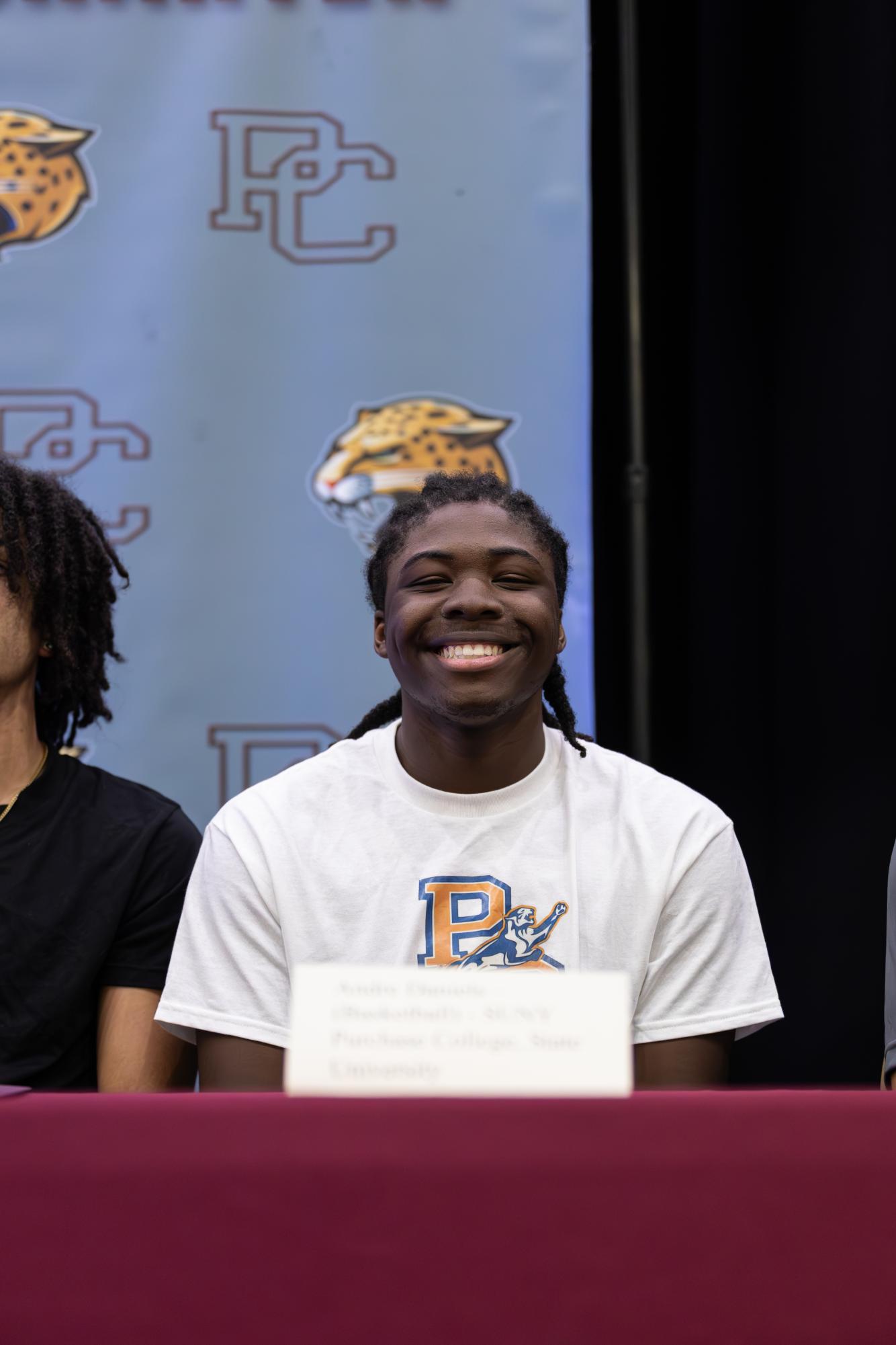 Senior Andre Daniels smiles at the camera with a shirt that represents his future college. 