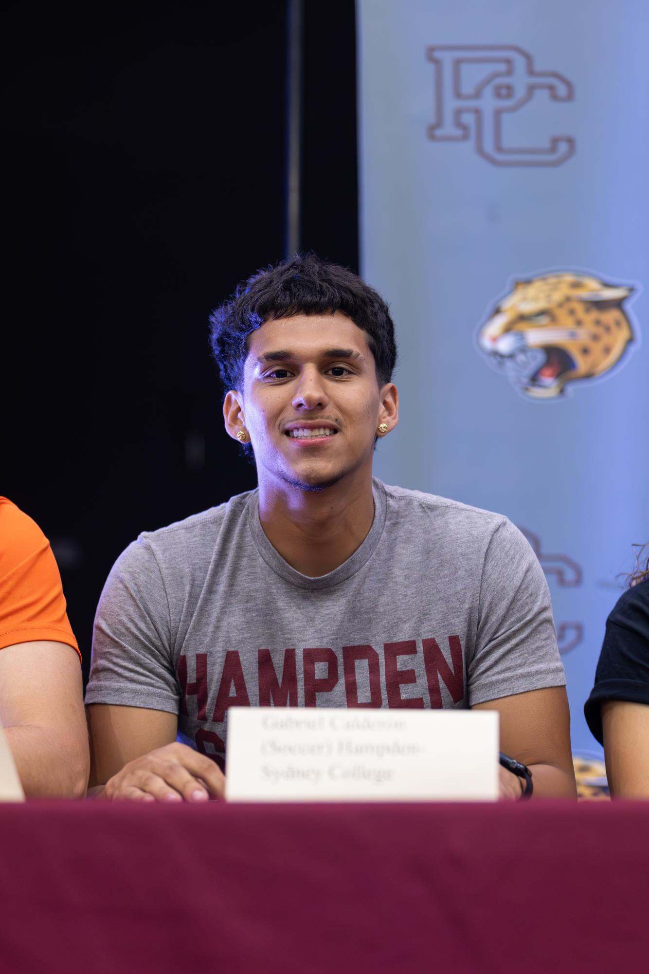 Senior Gabriel Calderón smiles at the camera with a shirt that says his future college's name on it. 