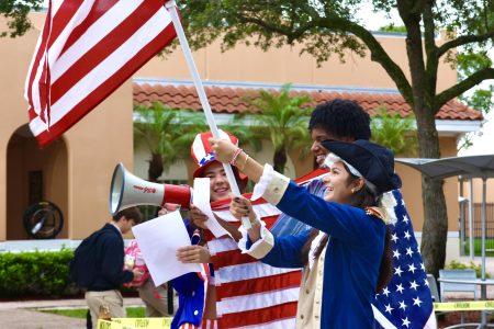 Seniors wave a giant American flag. One holds a megaphone for her recitation, while another is dressed as a Founding Father, white wig and all. Picture by: <a href="https://ppchsnews.com/staff_profile/evan-omana/">Evan Omana</a>