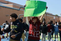 Senior Liz Rubio, who drew on her school uniform, holds up a sign that says, "No one is illegal on stolen land".