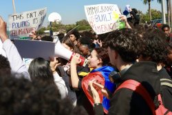 A student shouts in a megaphone while others walk across the basketball court, waving posters supporting Pembroke Pines' immigrant population.