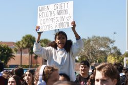 Sophomore Sarah Phelps-Hill sits on a student's shoulders and holds up a sign that reads, "When cruelty becomes normal, compassion becomes radical".